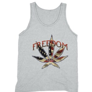 Puede incluir: Una camiseta sin mangas gris con un gráfico de una hoja de marihuana con el diseño de la bandera estadounidense y la palabra "FREEDOM" encima.