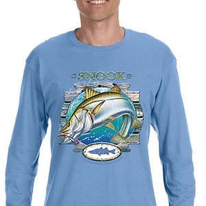 May include: Light blue long-sleeved t-shirt with a graphic of a snook fish jumping out of the water. The graphic includes the text "Snook" and a wooden plank background.
