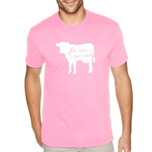 May include: Pink t-shirt featuring a white silhouette of a cow and the text "farm raised" in pink lettering.
