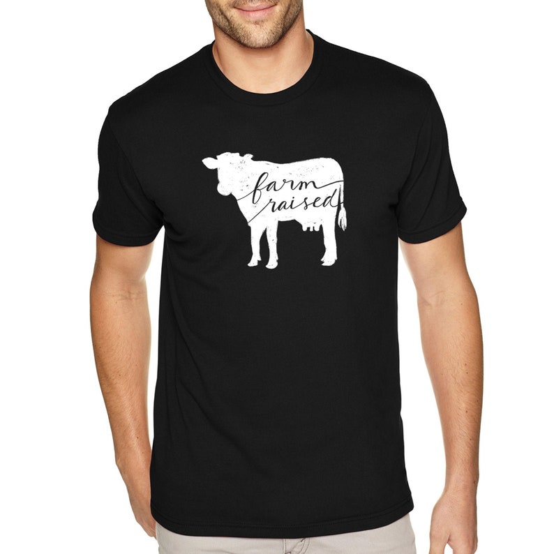 May include: A black t-shirt with a white silhouette of a cow and the text "farm raised" printed on the front.