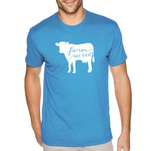 May include: A bright blue t-shirt with a white silhouette of a cow and the text "farm raised" printed on the front.