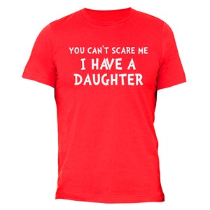 Puede incluir: Una camiseta roja con el texto blanco "YOU CAN'T SCARE ME I HAVE A DAUGHTER". La camiseta es de cuello redondo y parece estar hecha de un material suave.