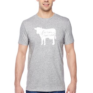 May include: A heather grey t-shirt with a white silhouette of a cow and the text "farm raised" written inside the cow.