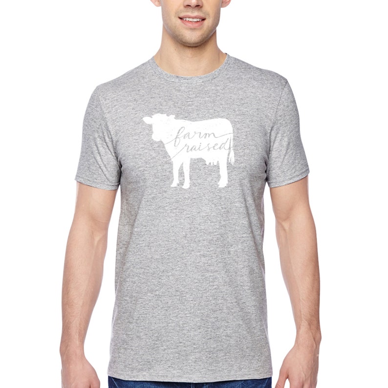 May include: A heather grey t-shirt with a white silhouette of a cow and the text "farm raised" written inside the cow.