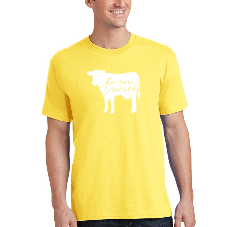 May include: A yellow t-shirt featuring a white silhouette of a cow with the text "farm raised" on the front.