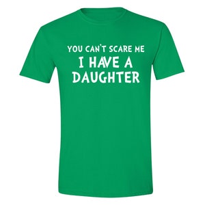 Puede incluir: Una camiseta verde con texto blanco que dice "YOU CAN'T SCARE ME I HAVE A DAUGHTER". La camiseta tiene mangas cortas y cuello redondo.