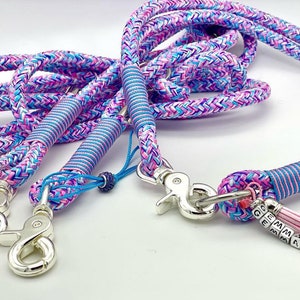 May include: A multi-strand braided rope leash featuring a vibrant pattern of pink, blue, and purple threads. The leash includes silver-toned metal swivel snap hooks, blue cord wrappings, and a personalized charm with the name GEMMA in beads.