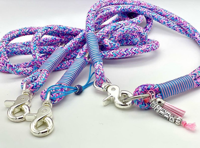 May include: A multi-strand braided rope leash featuring a vibrant pattern of pink, blue, and purple threads. The leash includes silver-toned metal swivel snap hooks, blue cord wrappings, and a personalized charm with the name GEMMA in beads.
