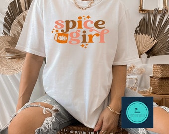 May include: White t-shirt with the text "spice girl" in orange and brown letters. A stylized mug with a pumpkin inside is next to the word "spice".