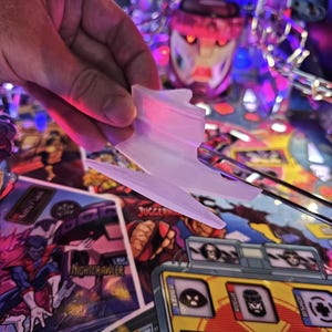 Op de afbeelding: Een witte plastic flipper met een paarse gloed. De flipper bevindt zich op een flipperkast met een kleurrijke achtergrond met personages uit de X-Men.