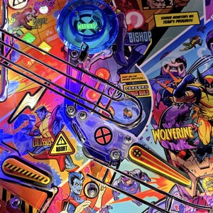 Op de afbeelding: Een flipperkast met een kleurrijk, stripboekachtig ontwerp met personages uit de X-Men. De machine heeft een blauwe en zilveren flipper, een waarschuwingsbord en een rood en geel gevaarlijk kamerbord. De machine heeft ook een Cerebro bonus build doel.