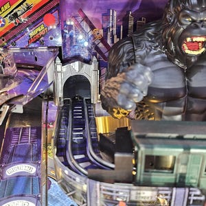 May include: A pinball machine with a King Kong theme. The game features a large gorilla figure, a cityscape backdrop, and a biplane graphic. The playfield includes ramps, tunnels, and a train car.