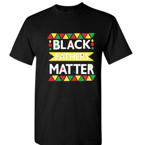 May include: Black t-shirt with a graphic design featuring the words "Black Fathers Matter" in yellow, red, and green. The design includes a pattern of triangles and circles.