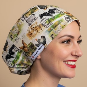 May include: A scrub cap featuring a farm-themed print with illustrations of cows, sheep, chickens, and geese on a light background. The fabric includes text reading Grains and Everyday Heroes on a small white label stitched to the side of the cap.