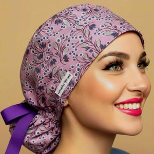 May include: A scrub cap in a dusty pink fabric featuring a repeating pattern of dark blue berries and light green leaves. The cap includes a white rectangular tag with the text Everyday Heroes and a solid purple ribbon tie at the back.