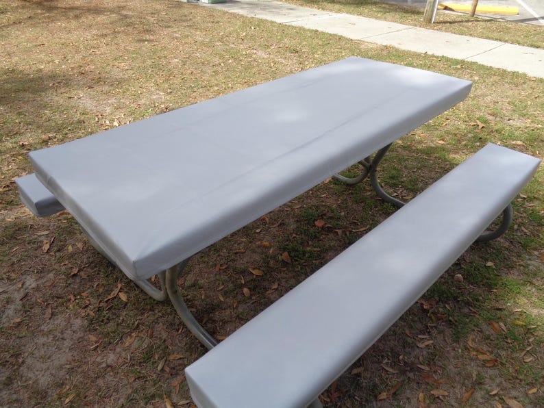 Puede incluir: Una cubierta de mesa de picnic gris con una cubierta de banco a juego. La cubierta est&aacute; hecha de un material impermeable y est&aacute; dise&ntilde;ada para proteger la mesa de los elementos.