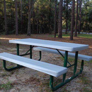 Puede incluir: Una cubierta de mesa de picnic gris con un marco de metal verde. La cubierta est&aacute; sobre una mesa de picnic en un &aacute;rea boscosa.