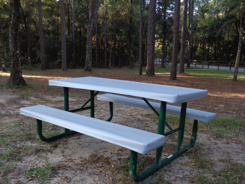 Puede incluir: Una cubierta de mesa de picnic gris con un marco de metal verde. La cubierta est&aacute; sobre una mesa de picnic en un &aacute;rea boscosa.