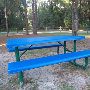 May include: A blue picnic table with a metal frame and a blue cover. The table is in a grassy area with trees in the background.