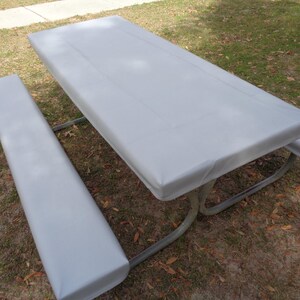 Puede incluir: Una cubierta de mesa de picnic gris con una cubierta de banco a juego. La cubierta est&aacute; hecha de un material impermeable y est&aacute; dise&ntilde;ada para proteger la mesa de los elementos.