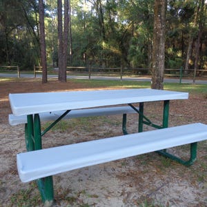 Puede incluir: Una mesa de picnic blanca con estructura de metal verde. La mesa y los bancos est&aacute;n cubiertos con una funda de tela blanca.