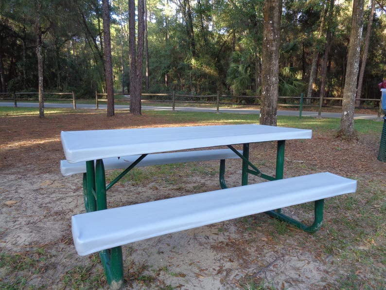 Puede incluir: Una mesa de picnic blanca con estructura de metal verde. La mesa y los bancos est&aacute;n cubiertos con una funda de tela blanca.