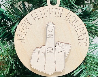 May include: A round wooden Christmas ornament with the text "Happy Flippin Holidays" and a middle finger graphic.
