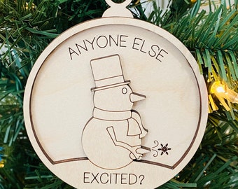 May include: A wooden Christmas ornament with a snowman design and the text "Anyone else excited?" The snowman is wearing a top hat and scarf and is blowing a snowflake.