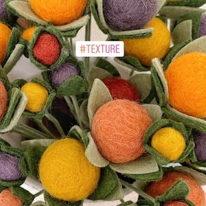 May include: A bouquet of felt flowers in various colors, including orange, yellow, red, purple, and green. The flowers are arranged in a vase and have a textured appearance. #TEXTURE