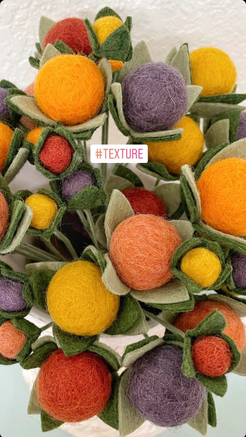May include: A bouquet of felt flowers in various colors, including orange, yellow, red, purple, and green. The flowers are arranged in a vase and have a textured appearance. #TEXTURE
