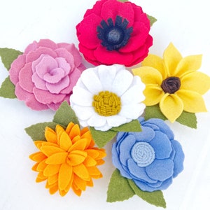 May include: A set of six felt flower embellishments in various colors and styles, including a red poppy, a pink rose, a white daisy, a yellow sunflower, a blue hydrangea, and an orange dahlia.