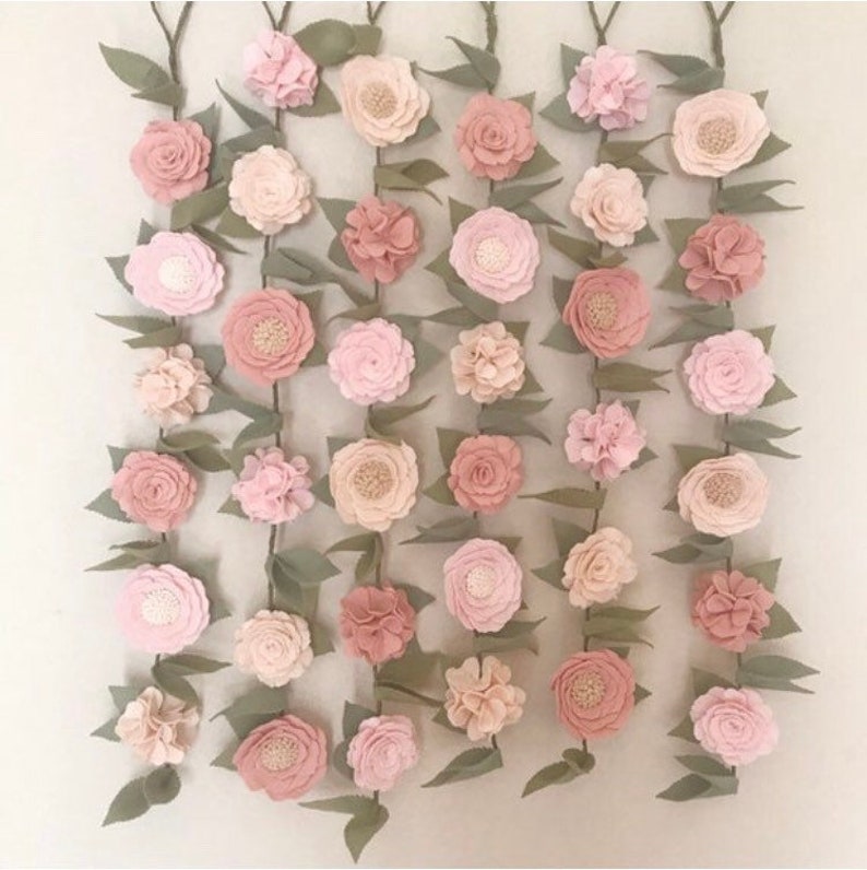 May include: A garland of felt flowers in shades of pink and green. The flowers are arranged in a cascading pattern, with the largest flowers at the top and the smallest flowers at the bottom.