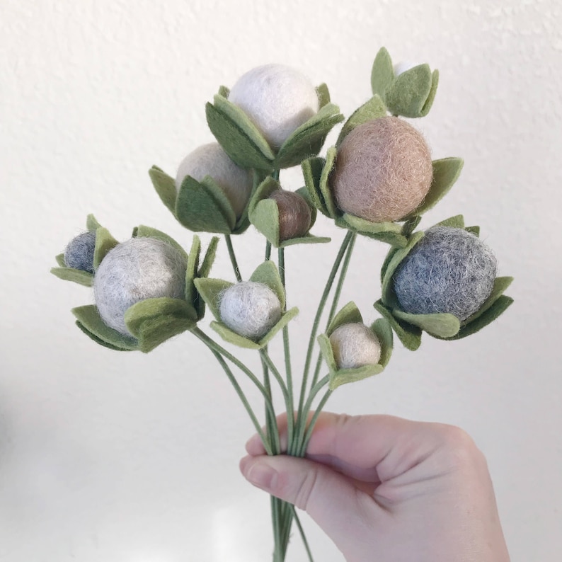May include: A bouquet of felt flowers with green leaves and white, brown, and gray felt balls.