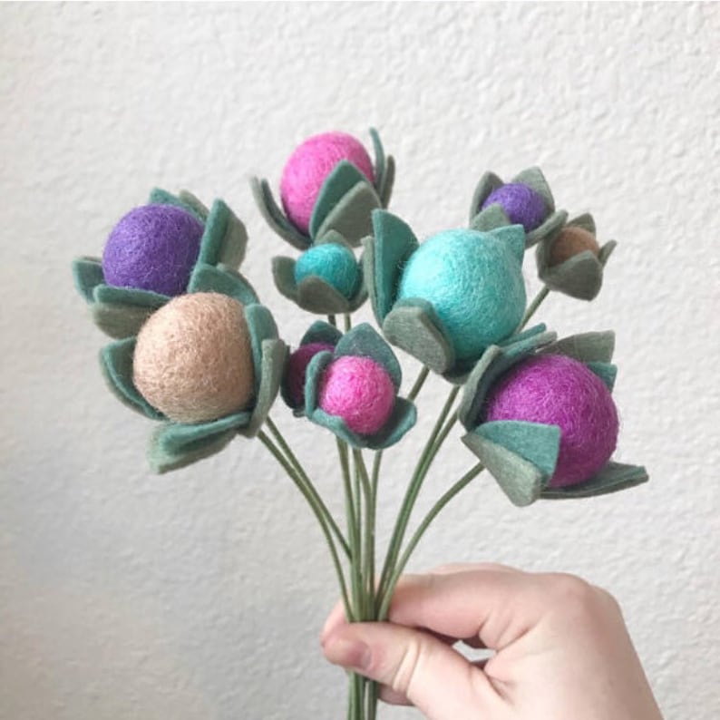 May include: A bouquet of felt flowers with green leaves and colorful felt balls in shades of pink, purple, teal, and beige.