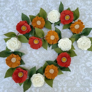 May include: A felt flower garland with orange, red, and white flowers. The garland is made of felt and is perfect for decorating a home or party.