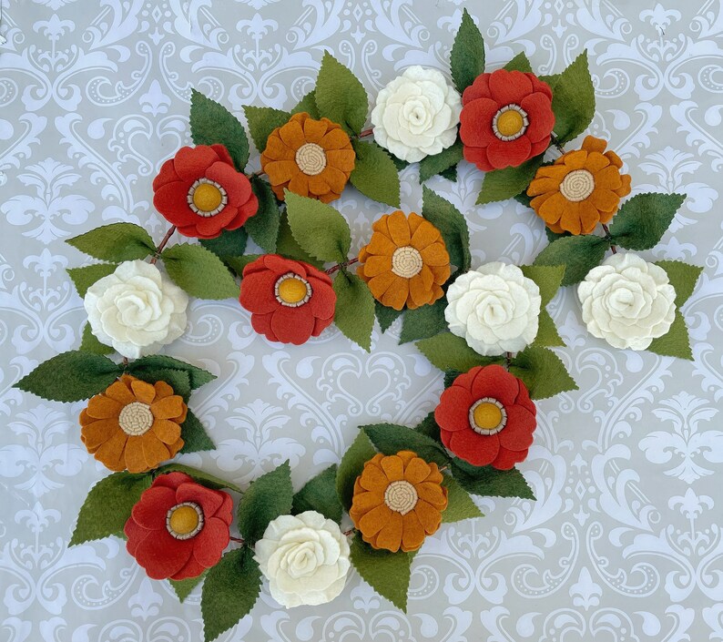 May include: A felt flower garland with orange, red, and white flowers. The garland is made of felt and is perfect for decorating a home or party.
