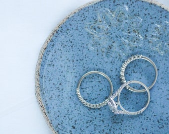 May include: Three silver rings on a blue ceramic ring dish with a floral design.