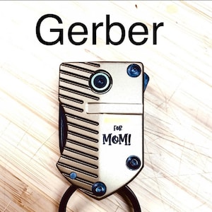May include: A gold-coloured Gerber multi-tool with a black ring and the words "for MOM!" on the front.