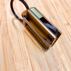 May include: A small, multi-tool keychain with a black ring, a green accent, and a bronze finish.