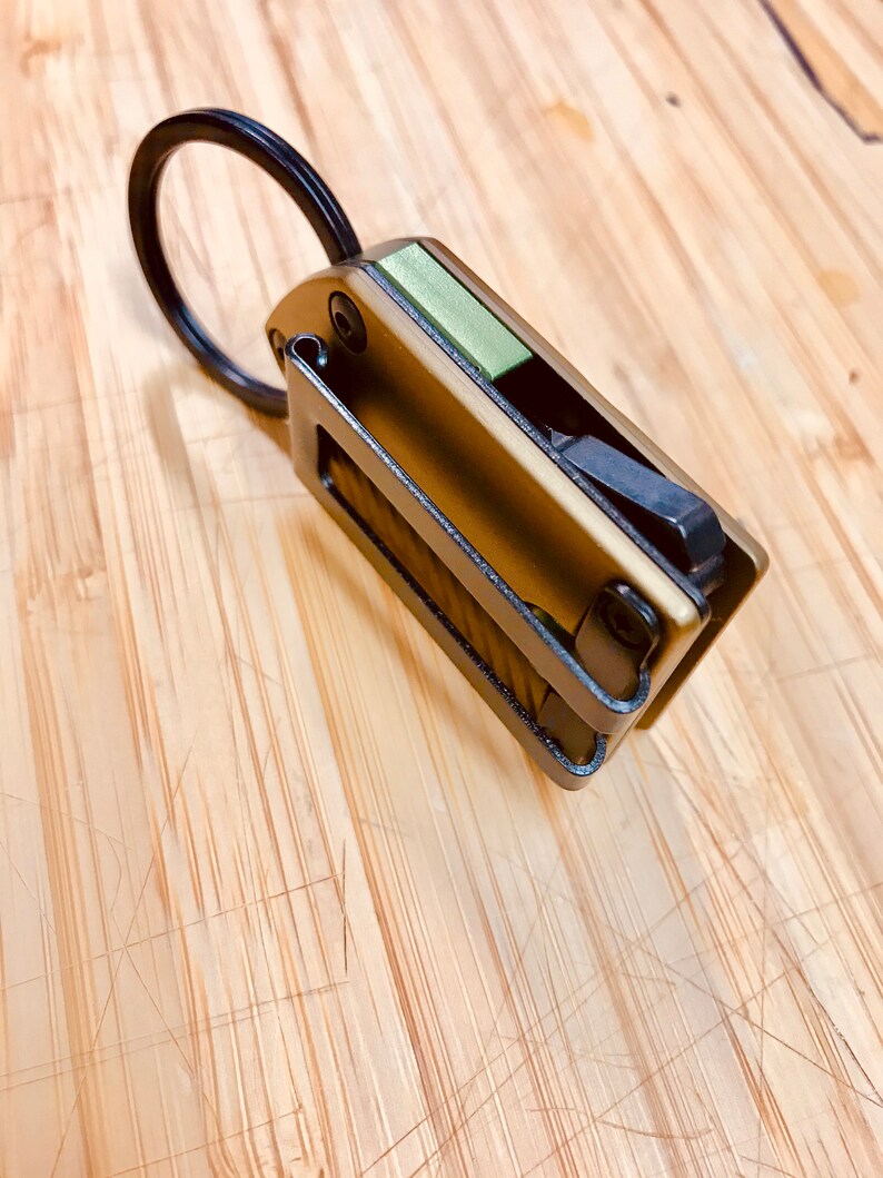 May include: A small, multi-tool keychain with a black ring, a green accent, and a bronze finish.