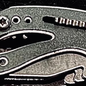 K&ouml;nnte beinhalten: Nahaufnahme eines silbernen Multitools mit einer strukturierten grauen Oberfl&auml;che. Das Werkzeug verf&uuml;gt &uuml;ber eine Vielzahl von Funktionen, darunter eine Klinge, eine Feile und einen Schraubendreher.