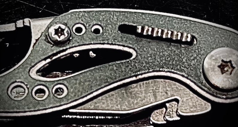 K&ouml;nnte beinhalten: Nahaufnahme eines silbernen Multitools mit einer strukturierten grauen Oberfl&auml;che. Das Werkzeug verf&uuml;gt &uuml;ber eine Vielzahl von Funktionen, darunter eine Klinge, eine Feile und einen Schraubendreher.