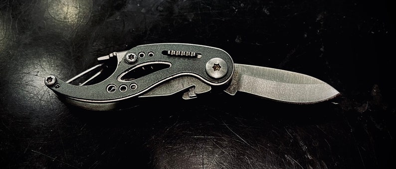 K&ouml;nnte beinhalten: Ein schwarzes Multifunktions-Taschenmesser mit einer silbernen Klinge und einer Vielzahl von Werkzeugen, darunter ein Flaschen&ouml;ffner, ein Schraubendreher und eine Feile.