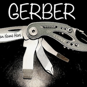 Pode incluir: Uma multiferramenta Gerber prateada com cabo preto e uma variedade de ferramentas, incluindo uma faca, alicates e uma chave de fenda. A ferramenta é gravada com o texto "Groomysman Name Here".