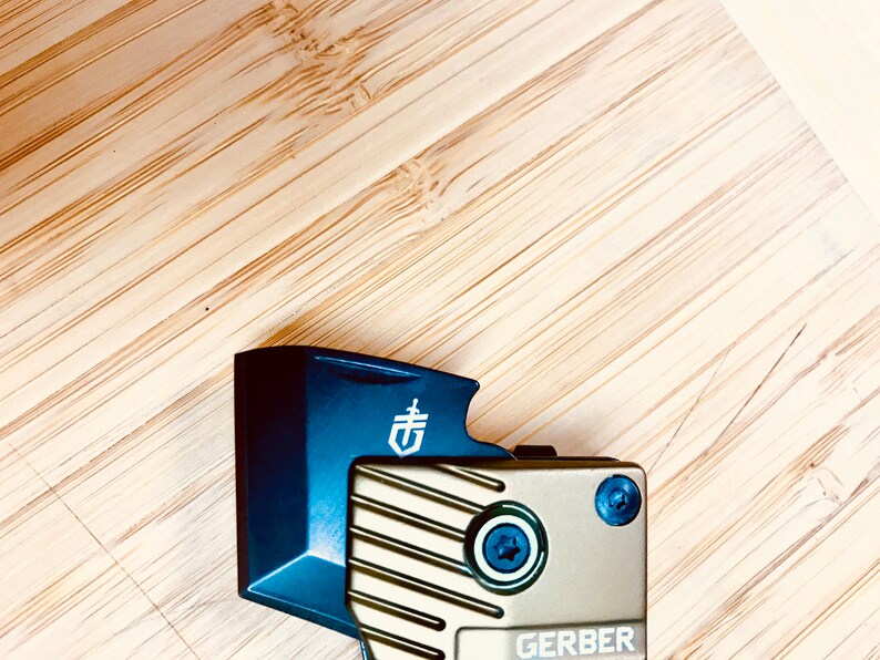 May include: A blue and gold multi-tool with a Gerber logo. The tool has a textured surface and a black screw.