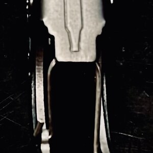 K&ouml;nnte beinhalten: Nahaufnahme eines silbernen Flaschen&ouml;ffners, der an einem schwarzen Lederband befestigt ist. Der Flaschen&ouml;ffner hat oben eine kleine, erhabene Flaschenform.