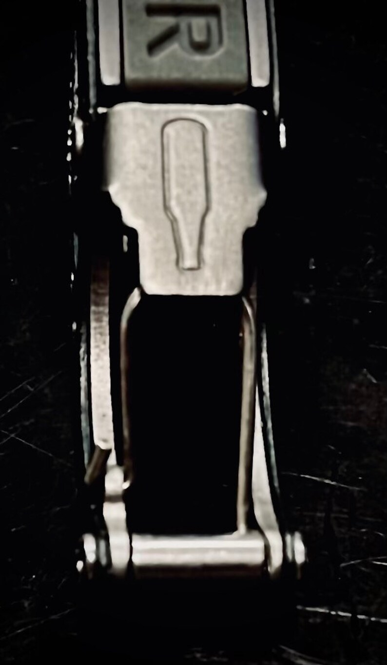 K&ouml;nnte beinhalten: Nahaufnahme eines silbernen Flaschen&ouml;ffners, der an einem schwarzen Lederband befestigt ist. Der Flaschen&ouml;ffner hat oben eine kleine, erhabene Flaschenform.