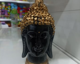 May include: Black and gold Buddha head statue with a golden crown. The statue is made of a smooth, polished material.