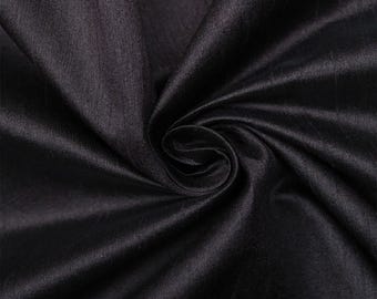 May include: Close-up of a smooth, black fabric with a subtle sheen. The fabric is draped and folded, creating soft, flowing lines.