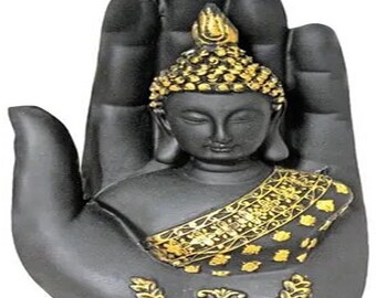May include: A black Buddha statue with gold accents, cradled in a black hand. The Buddha has a serene expression, a gold headdress, and a gold-patterned shawl. Decorative gold embellishments adorn the base of the statue.